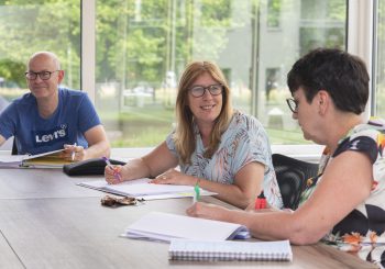 Drie volwassenen aan tafel pratend met elkaar